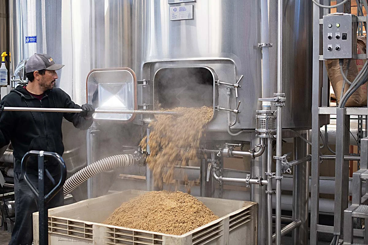 Brewer Brian Edwards filling a bin with spent grain for Bianchi Ranch