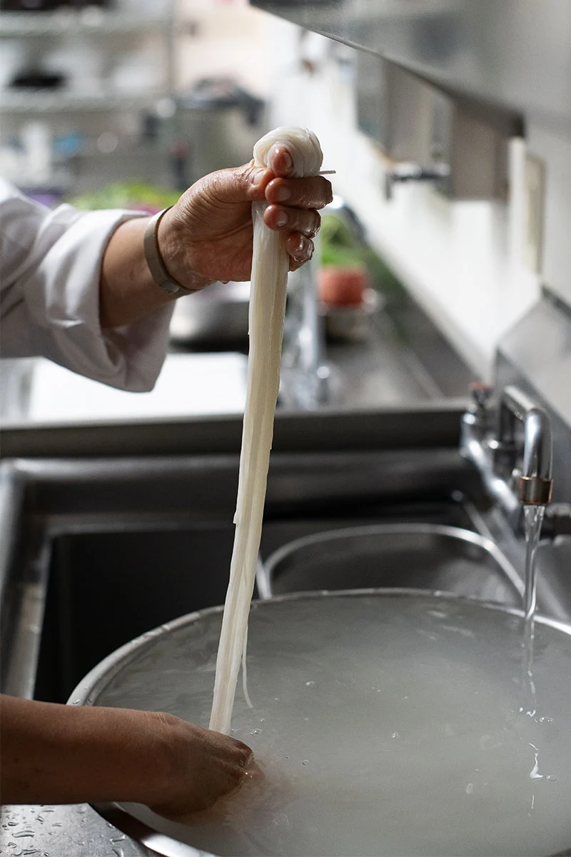 Long rice noodles being pulled and drained before forming into a nest